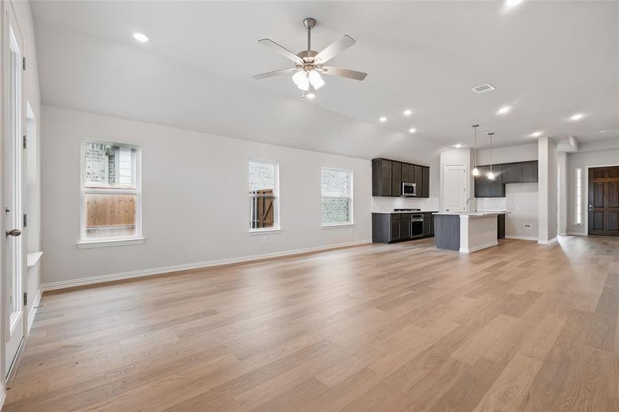 Unfurnished living room with healthy amount of natural light, ceiling fan, baseboards, vaulted ceiling, and recessed lighting Unfurnished living room with healthy amount of natural light, ceiling fan, baseboards, vaulted ceiling, and recessed lighting