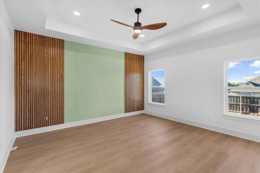 Unfurnished room with light hardwood / wood-style floors, ceiling fan, and a raised ceiling