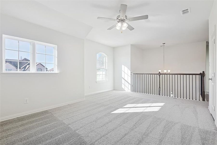 Carpeted spare room featuring ceiling fan with notable chandelier and plenty of natural light