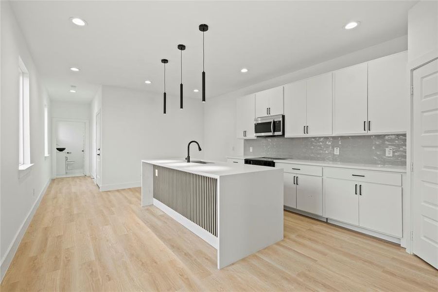 Kitchen with stainless steel microwave, light wood finished floors, tasteful backsplash, a center island with sink, and recessed lighting Kitchen with stainless steel microwave, light wood finished floors, tasteful backsplash, a center island with sink, and recessed lighting