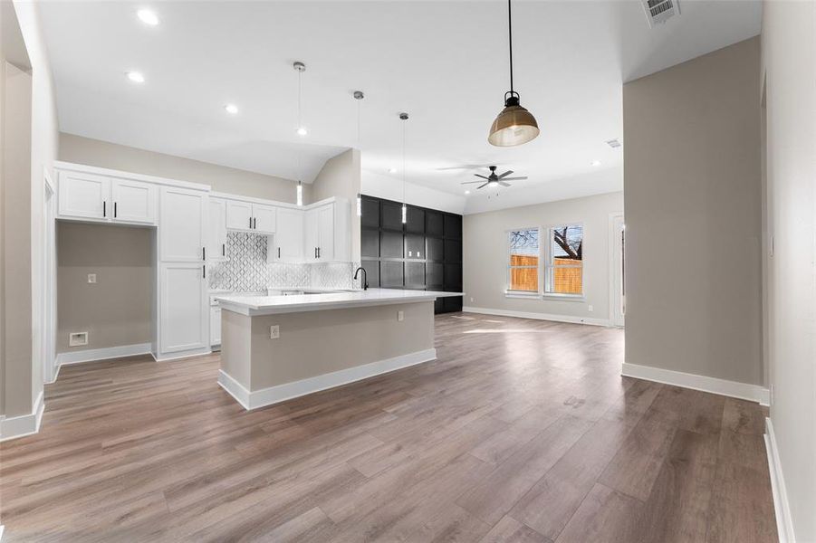 Kitchen with decorative light fixtures, an island with sink, white cabinets, backsplash, and light hardwood / wood-style floors