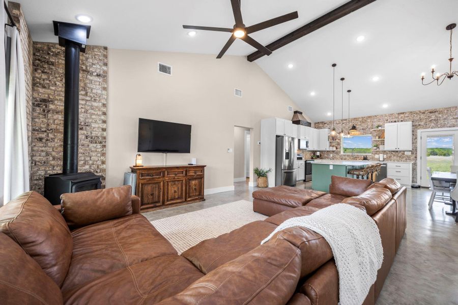 Living room with ceiling fan, finished concrete floors, a chandelier, a wood stove, and vaulted ceiling