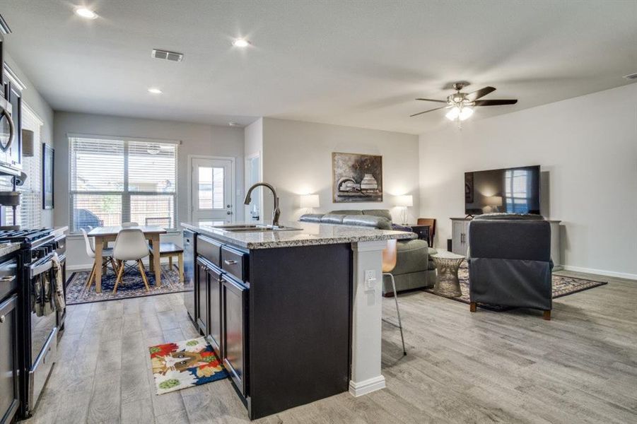 Kitchen with light wood finished floors, open floor plan, a breakfast bar area, stainless steel appliances, and a sink