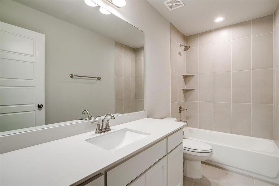 Full bathroom with tiled shower / bath combo, vanity, tile patterned floors, and toilet