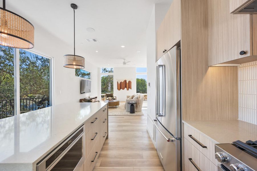 Contemporary kitchen featuring a large island with integrated microwave, stainless steel appliances, light wood-finish cabinetry, and white tile backsplash