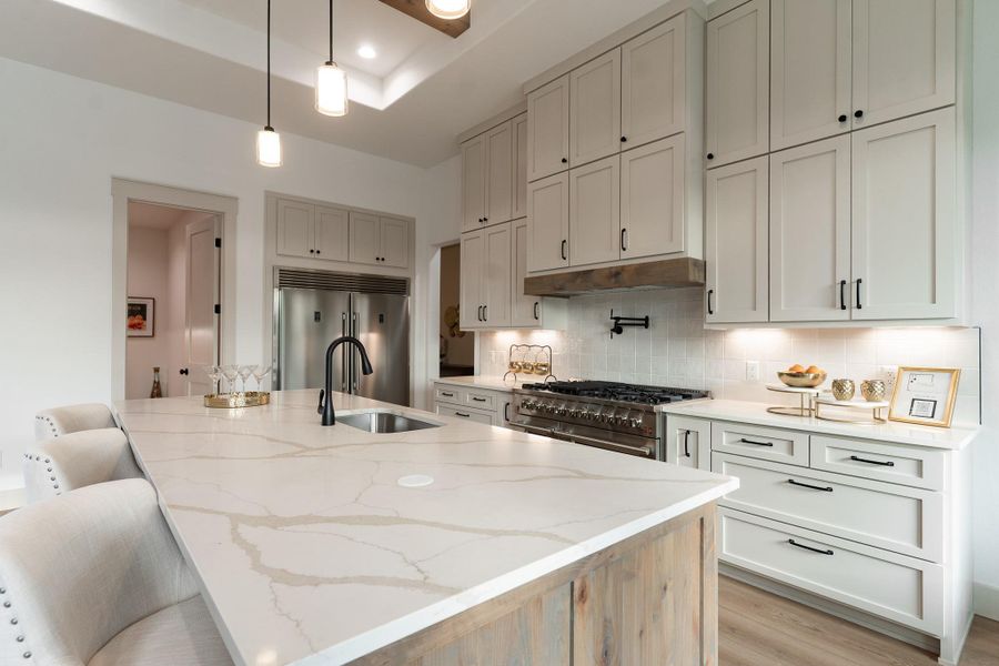 Kitchen featuring high end appliances, light stone countertops, backsplash, pendant lighting, and light wood finished floors Kitchen featuring high end appliances, light stone countertops, backsplash, pendant lighting, and light wood finished floors