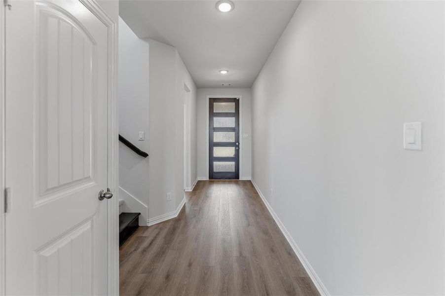 Entryway featuring wood-finish flooring, white baseboards, recessed ceiling lights, a modern front door with frosted glass panels, and a staircase with a dark handrail