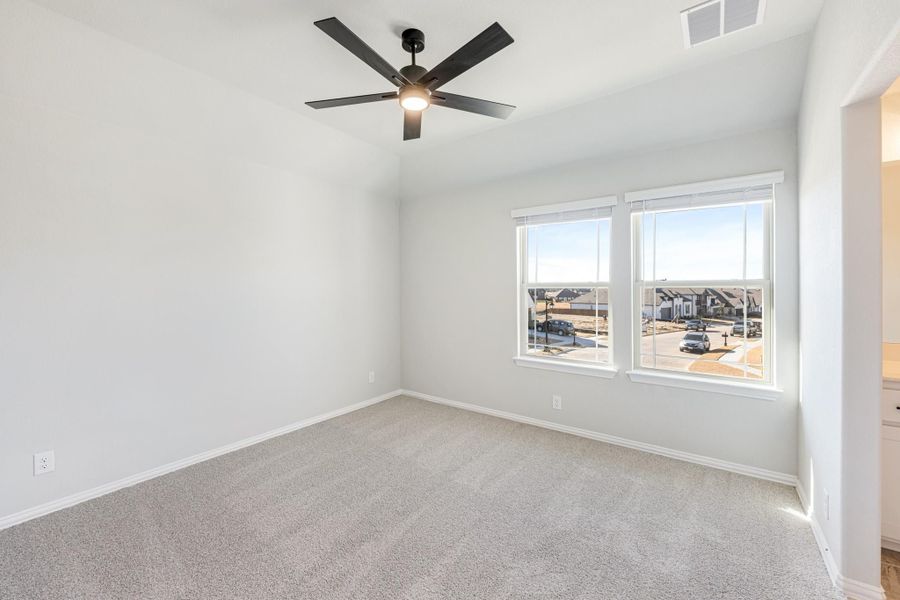 Empty bedroom with gray carpet, ceiling fan, and double windows overlooking a neighborhood street Empty bedroom with gray carpet, ceiling fan, and double windows overlooking a neighborhood street