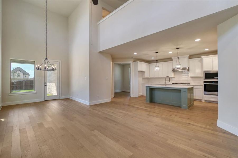 Kitchen with open floor plan, suspended lighting, an island with sink, dual tone cabinets, and a high ceiling Kitchen with open floor plan, suspended lighting, an island with sink, dual tone cabinets, and a high ceiling