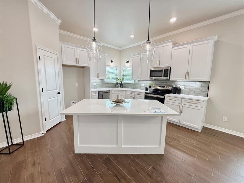 Kitchen featuring white cabinets, a center island, backsplash, appliances with stainless steel finishes, and pendant lighting Kitchen featuring white cabinets, a center island, backsplash, appliances with stainless steel finishes, and pendant lighting