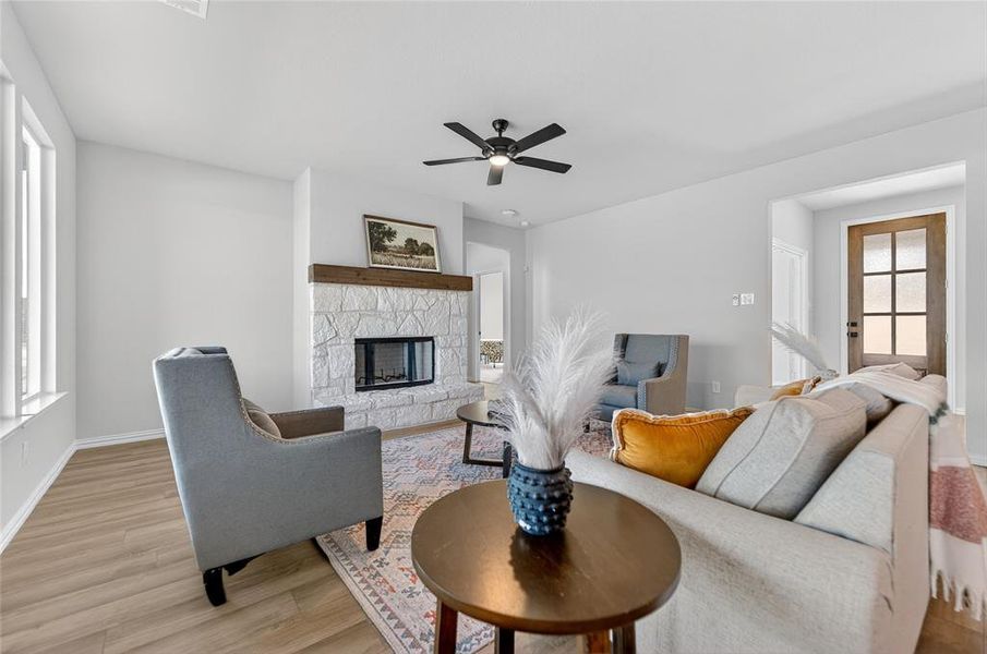 Living room featuring light wood-style floors, a ceiling fan, and a stone fireplace Living room featuring light wood-style floors, a ceiling fan, and a stone fireplace