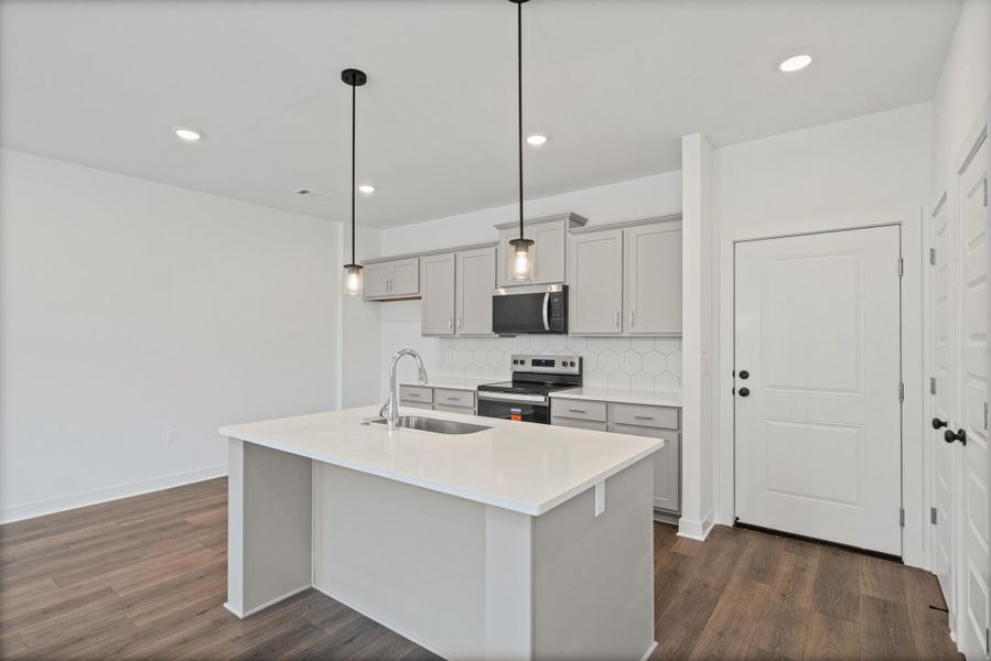 Kitchen featuring an island with sink, pendant lighting, built-in microwave, and wood-finish flooring