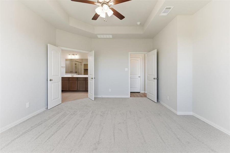 Unfurnished bedroom with light carpet, a raised ceiling, a ceiling fan, and connected bathroom