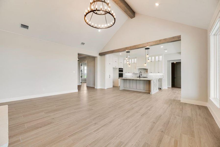 Unfurnished living room with beamed ceiling, high vaulted ceiling, a chandelier, and light wood-type flooring Unfurnished living room with beamed ceiling, high vaulted ceiling, a chandelier, and light wood-type flooring