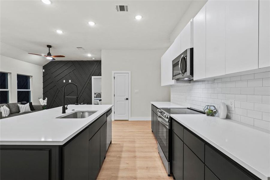 Kitchen featuring sink, white cabinetry, stainless steel appliances, and an island with sink