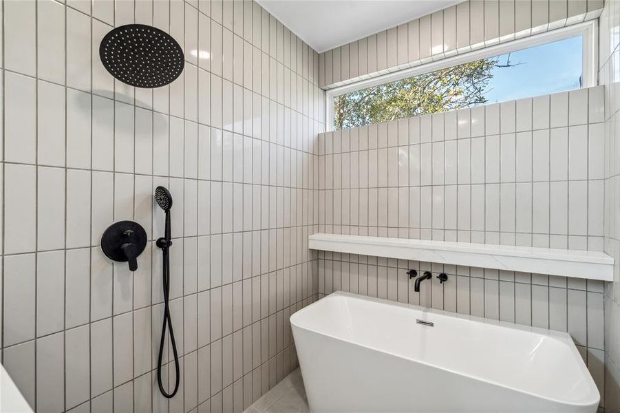 Modern shower and bath combination featuring a sleek freestanding soaking tub, rainfall showerhead, and floor-to-ceiling contemporary tile design with a clerestory window for natural light and privacy.