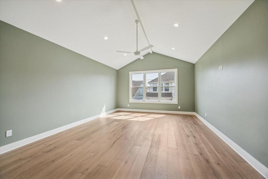 Primary bedroom retreat showcases vaulted ceilings and a statement sage accent wall that adds warmth and architectural interest. Wide plank hardwood floors and a large picture window fill the space with natural light, creating a calm, elevated escape upstairs.