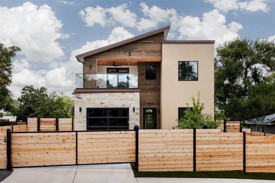 A striking blend of stone, wood, and stucco creates a bold, modern facade, framed by a natural wood gate and fence, offering both sophistication and privacy.