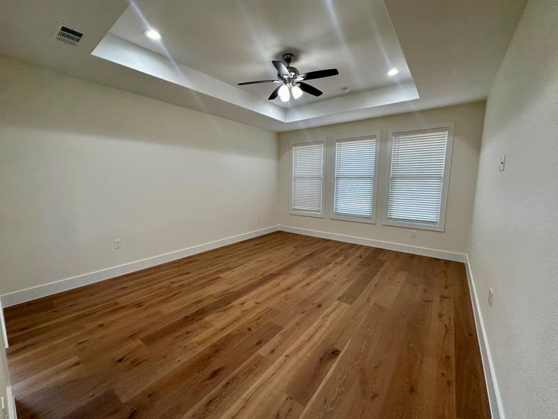 Unfurnished room featuring a raised ceiling, dark wood finished floors, and a ceiling fan