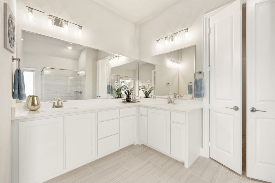 Master bathroom with dual sinks, white L-shaped vanity, large mirrors, and light tile floors