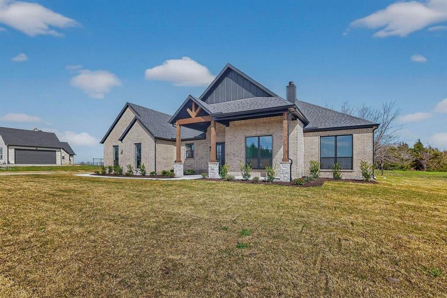 View of front of property with a front yard, brick siding, covered porch, a chimney, and board and batten siding