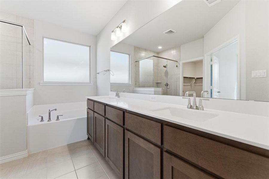 Full bath featuring a spacious closet, double vanity, a stall shower, a bath, and light tile patterned flooring