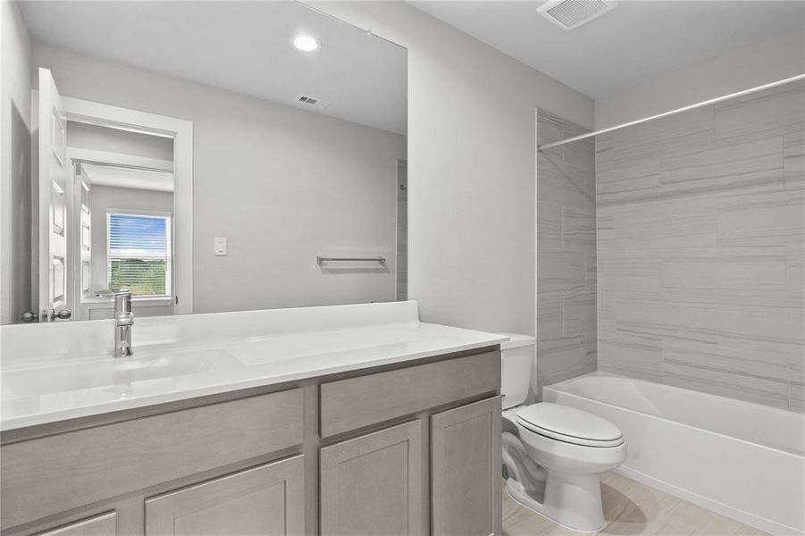 Secondary bath features tile flooring, bath/shower combo with tile surround, stained cabinets, beautiful light countertops, mirror, sleek fixtures and modern finishes.