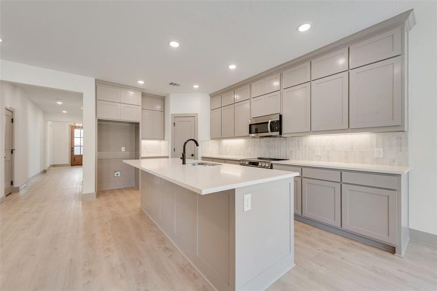 Kitchen with tasteful backsplash, sink, a center island with sink, and gray cabinetry