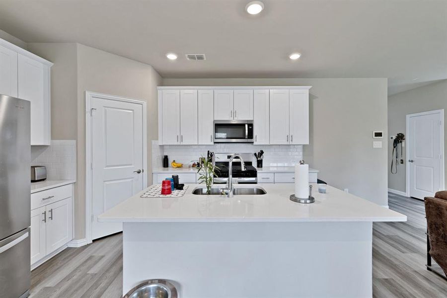 The kitchen features white cabinetry, a large kitchen island with an integrated sink, stainless steel appliances, and wood-look flooring