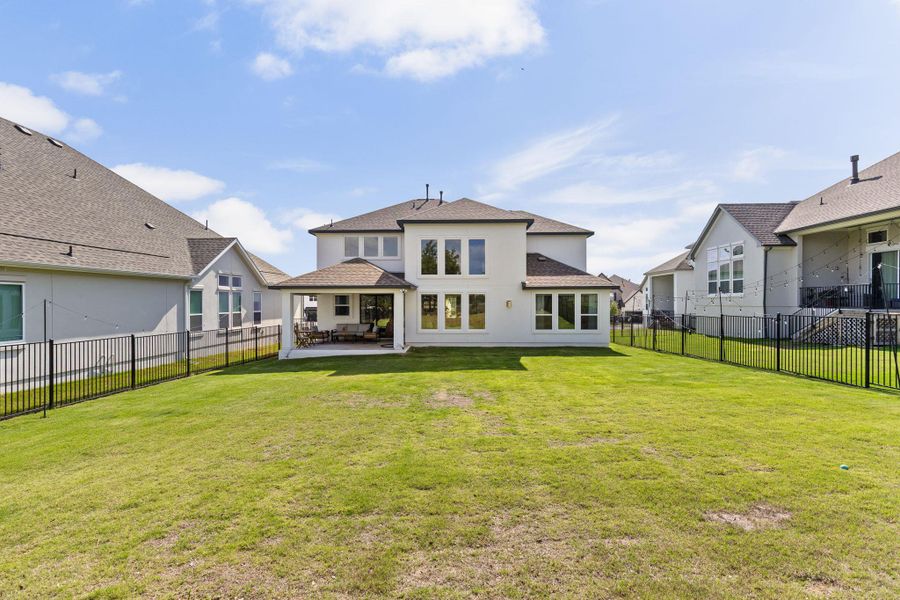 Spacious backyard featuring a manicured lawn, a covered patio, and perimeter fencing