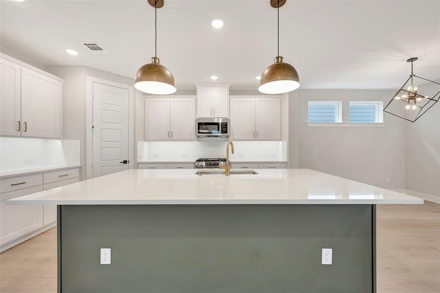 Two tone kitchen with light wood-type flooring, a kitchen island with sink, two tone color scheme, stainless steel appliances, and light stone countertops