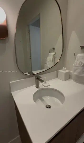 Wall-mounted vanity featuring a quartz countertop, integrated circular sink, metallic single-handle faucet, and an organically shaped mirror with a metallic frame