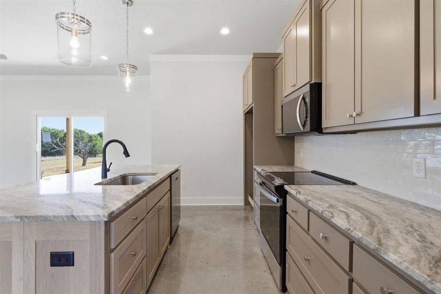 Kitchen with finished concrete floors, appliances with stainless steel finishes, light stone countertops, hanging light fixtures, and decorative backsplash