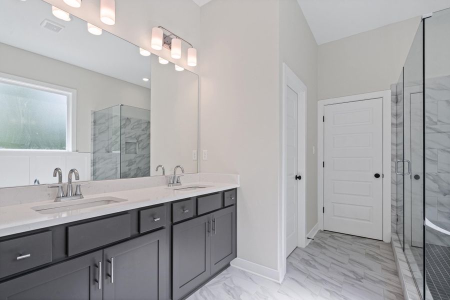 Full bath featuring light marble finish floors, double vanity, and a marble finish shower Full bath featuring light marble finish floors, double vanity, and a marble finish shower