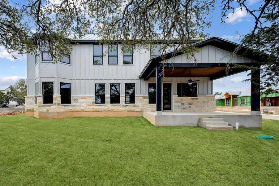 Rear view of property with board and batten siding, stone siding, a lawn, and ceiling fan