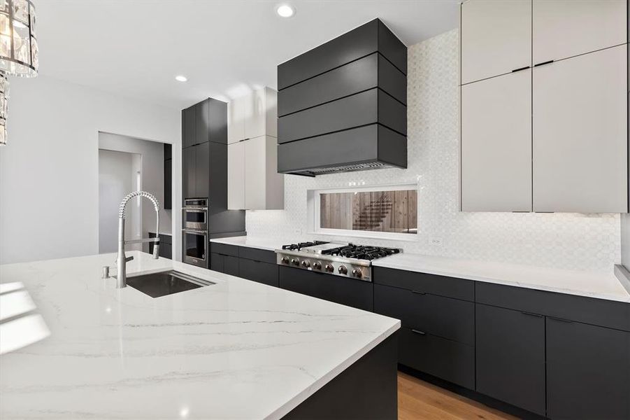 Kitchen with light stone counters, custom range hood, stainless steel appliances, sink, and white cabinets