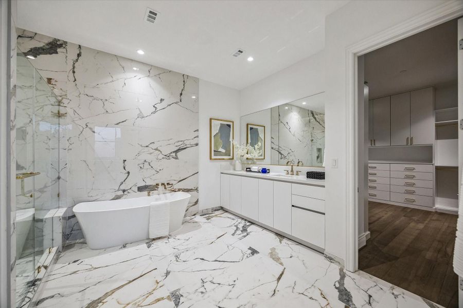 One of two primary baths, this space features large-format porcelain surfaces, a freestanding soaking tub, and a glass-enclosed shower, accented by French gold faucets and bath accessories. Both baths are thoughtfully separated by an expansive walk-in closet for added privacy and functionality.
