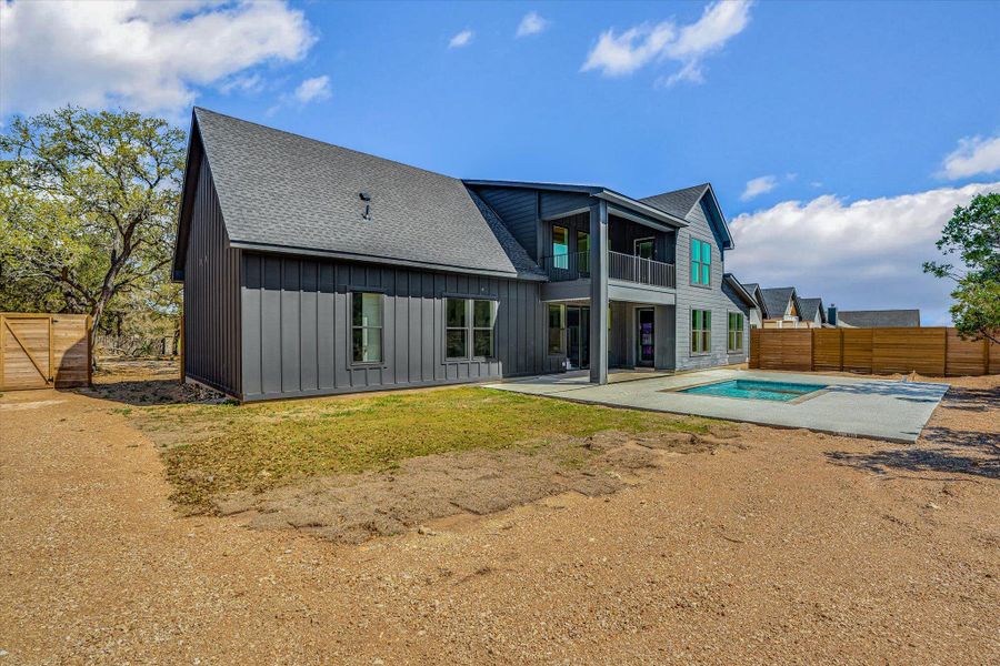 Rear view of property featuring board and batten siding, a patio area, a fenced backyard, roof with shingles, and a balcony