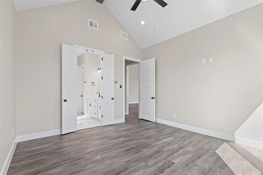 Unfurnished bedroom with hardwood / wood-style floors, ensuite bathroom, high vaulted ceiling, and ceiling fan