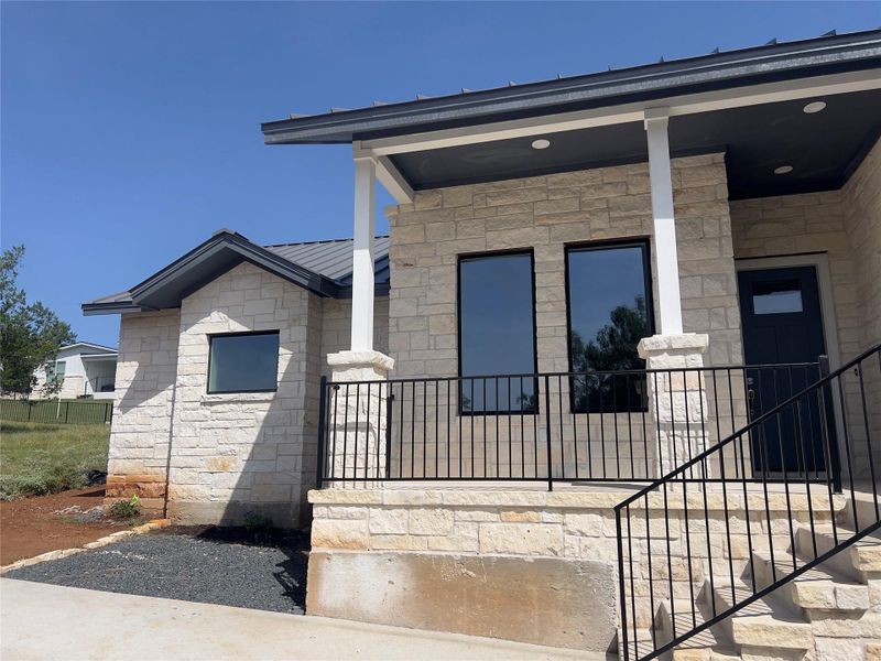 A newly constructed stone-clad residence showcases a welcoming porch and a sleek metal roof.