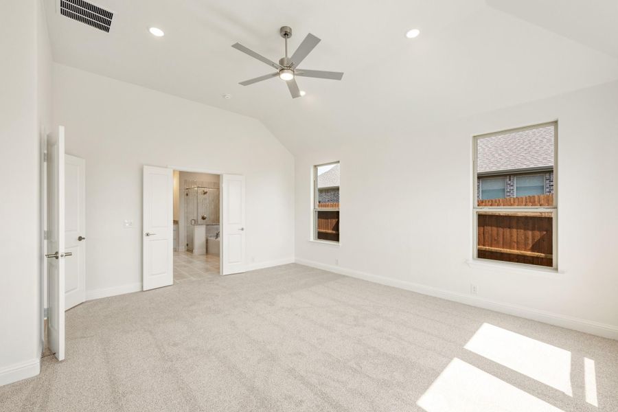 Spacious bedroom with vaulted ceiling, ceiling fan, carpet flooring, and ensuite bathroom doorway Spacious bedroom with vaulted ceiling, ceiling fan, carpet flooring, and ensuite bathroom doorway