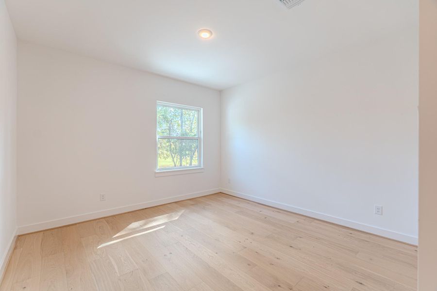 This room features bright natural light from a window, light wood flooring, and clean white walls, offering a blank canvas for personalization.