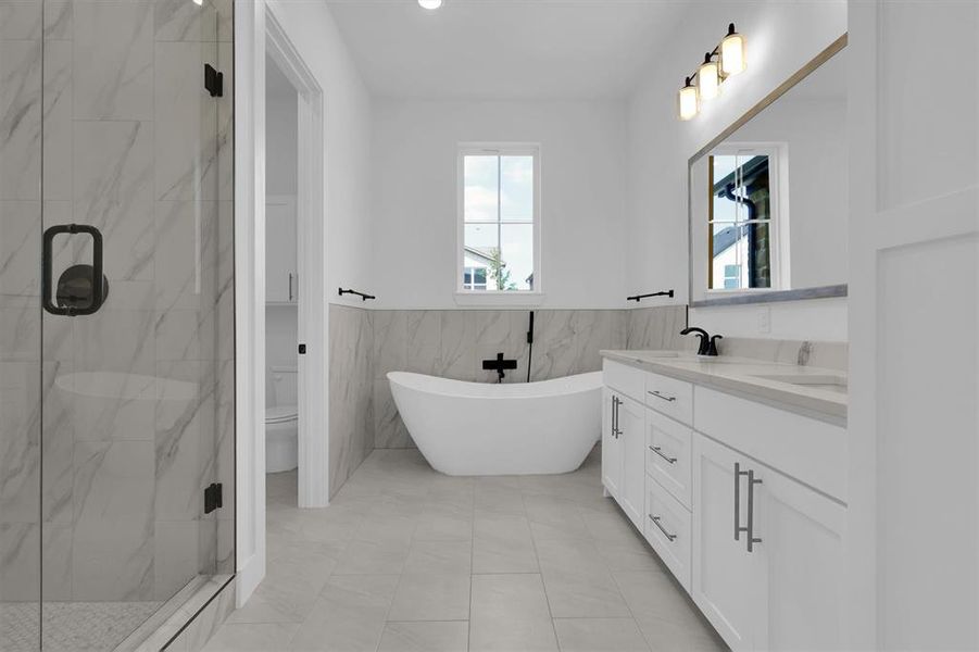 Full bathroom featuring double vanity, a marble finish shower, tile walls, a freestanding tub, and wainscoting Full bathroom featuring double vanity, a marble finish shower, tile walls, a freestanding tub, and wainscoting