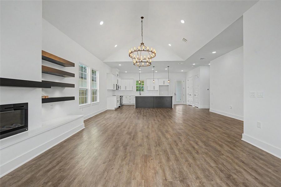 Living area features a sleek fireplace, floating shelves, vaulted ceiling, and abundant natural light.