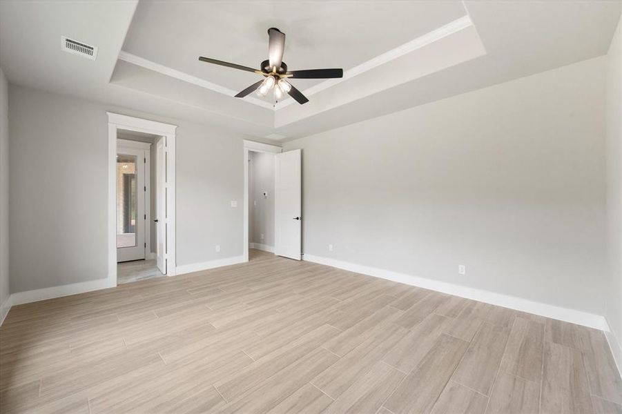 Spacious interior featuring wood-look tile flooring, light gray walls, a tray ceiling with crown molding, and a modern ceiling fan