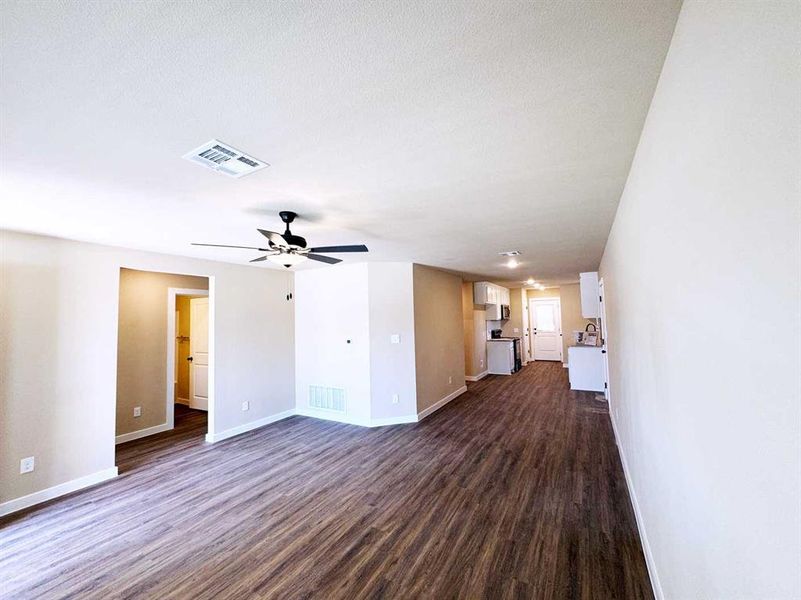 Unfurnished living room featuring baseboards, a ceiling fan, visible vents, and dark wood-type flooring
