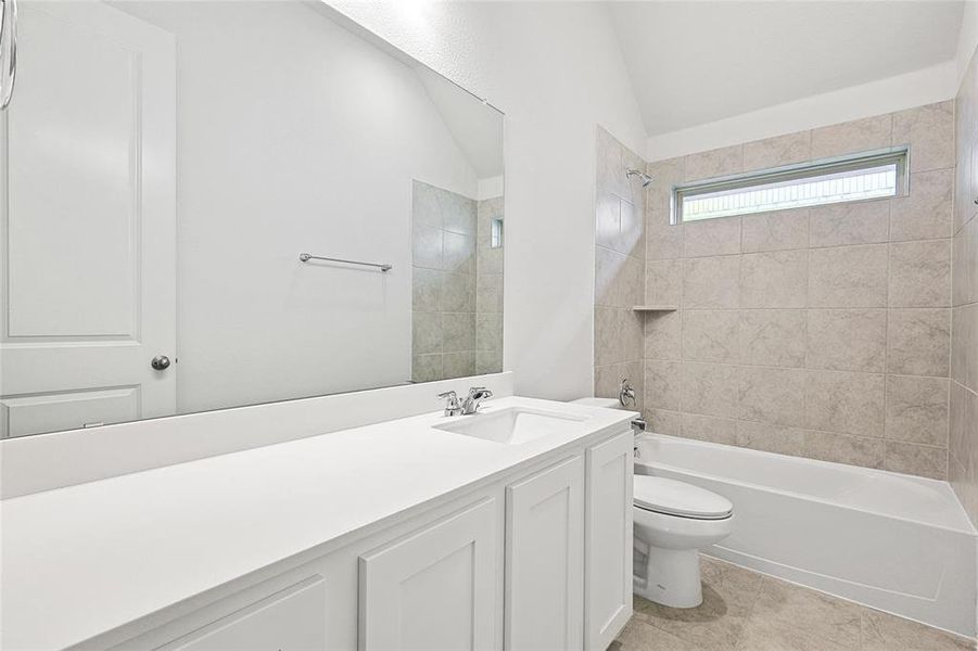 Full bathroom featuring tile patterned flooring, tiled shower / bath, toilet, vanity, and vaulted ceiling