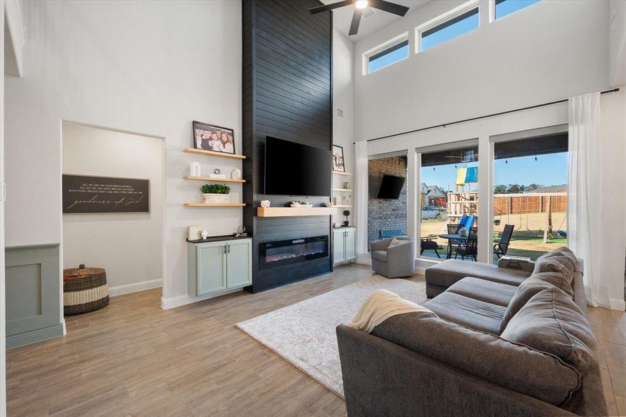 Living area featuring a towering ceiling, light wood-style floors, a large fireplace, and ceiling fan