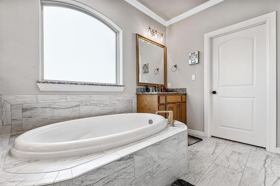 Bathroom with vanity, a relaxing tiled tub, and crown molding