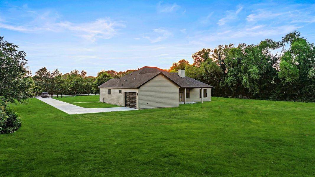 This photo showcases a single-story home with a spacious yard, and a long driveway leading to an attached garage, offering a serene and private setting. This photo showcases a single-story home with a spacious yard, and a long driveway leading to an attached garage, offering a serene and private setting.